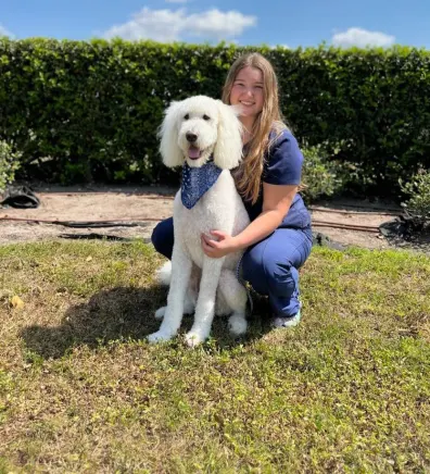 Samantha, groomer at Woofdorf Astoria of Lakewood Ranch, posing with white dog